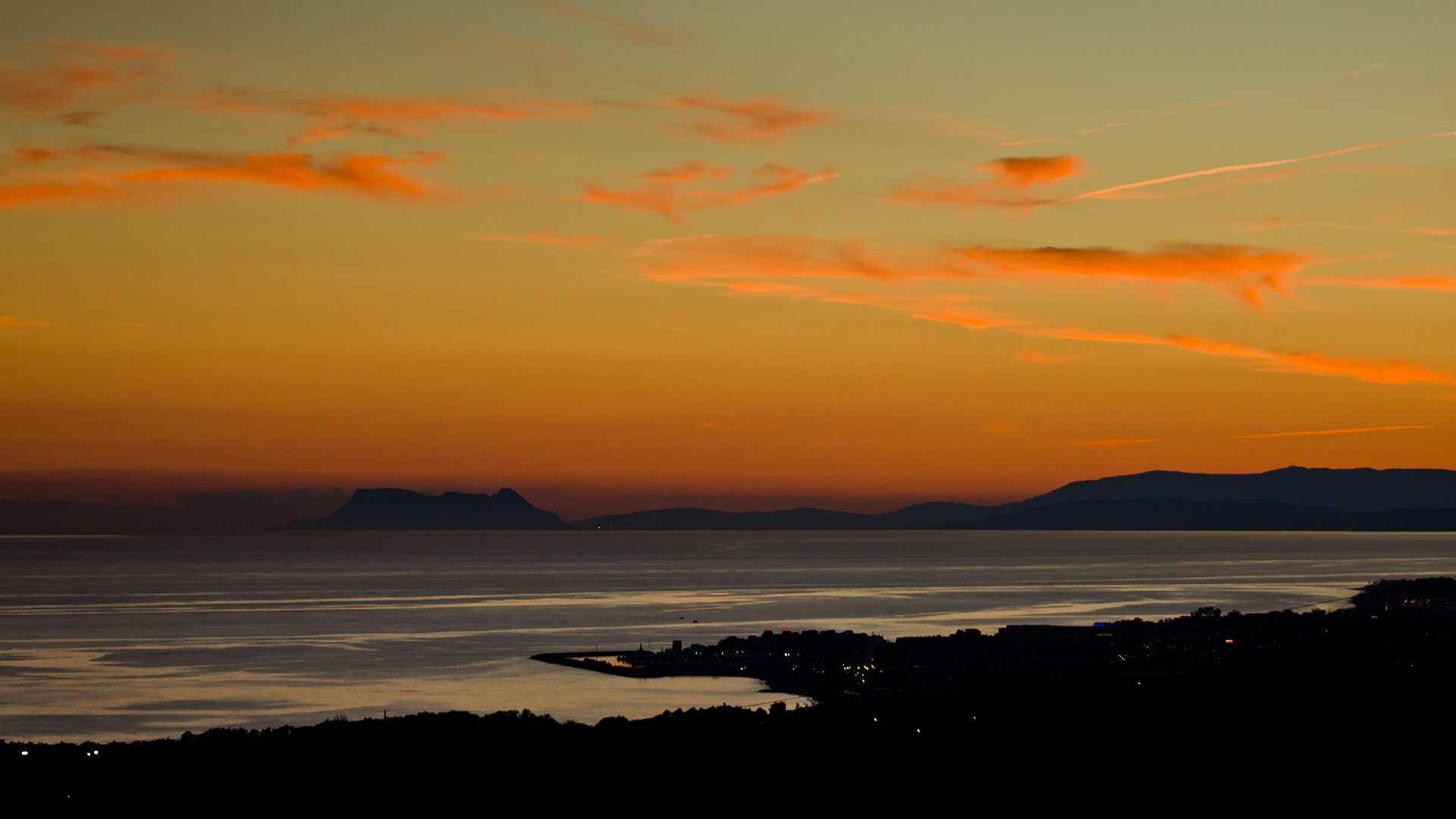 The sea at sunset on the Costa del Sol, the mountains dark against an orange sky